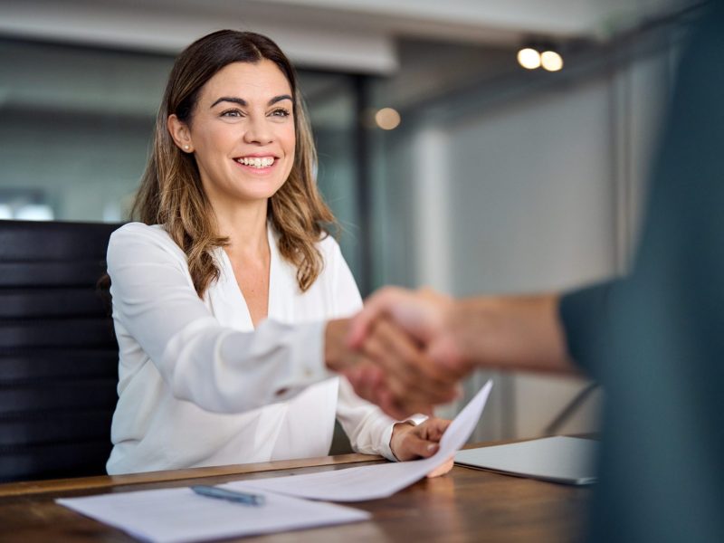 Happy mid aged business woman manager handshaking at office meeting. Smiling female hr hiring recruit at job interview, bank or insurance agent, lawyer making contract deal with client at work.
